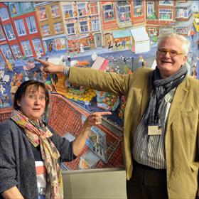 Charlotte Dematons (illustrator) wijst naar René Hollaers (Van Kemenade &amp; Hollaers). Hollaers&#39; wijst naar zijn winkel in Breda, op Dematons&#39; illustratie.