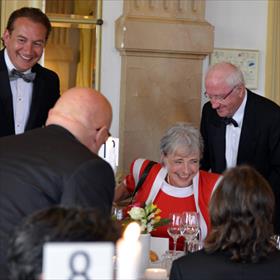Clairy Polak (juryvoorzitter) wordt door alle heren aan haar tafel tot zitten gebracht.